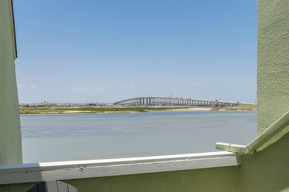 Scenic waterfront view featuring a distinctive arched bridge spanning across calm waters under clear blue skies.