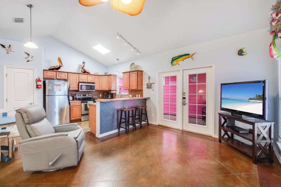 Relax in your bright, open-concept space where a fully equipped kitchen flows seamlessly into your comfortable living area with tropical beach scenes on the TV.
