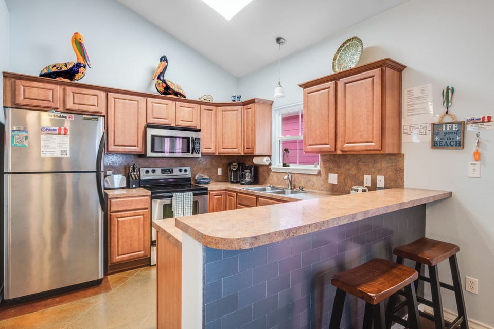 Your fully equipped kitchen invites culinary adventures with warm wood cabinets, stainless steel appliances, and a welcoming breakfast bar for morning coffee.