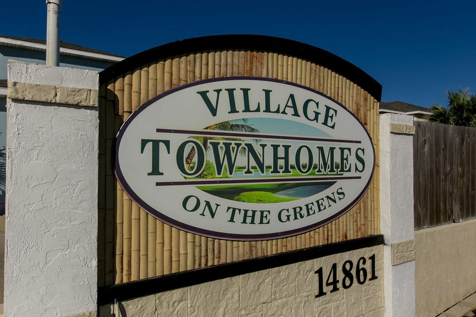 Property entrance sign for Village Townhomes on the Greens with clear address marking and decorative stone and bamboo design elements.