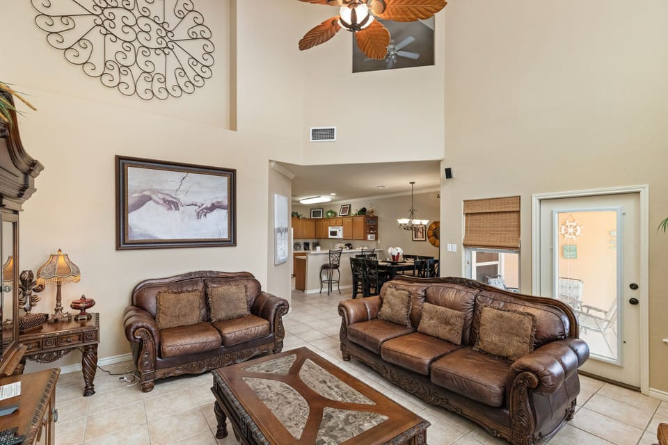 Relax in your spacious living room with vaulted ceilings, rich leather sofas, and tropical ceiling fan creating the perfect atmosphere.