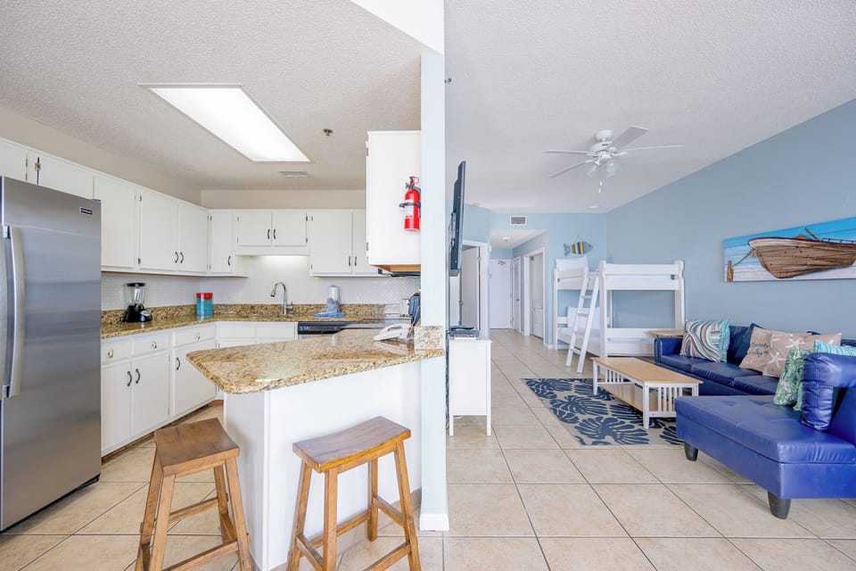 The modern kitchen features stainless appliances, granite countertops, and a cozy breakfast bar with wooden stools
