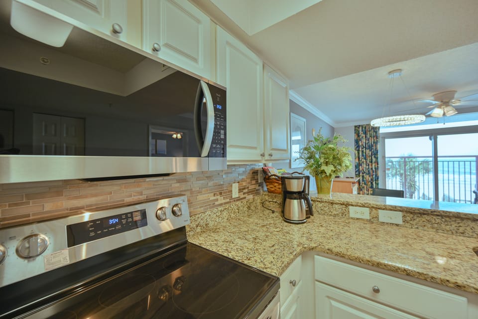 Modern kitchen with granite tops, white cabinets, and ocean-view dining area.