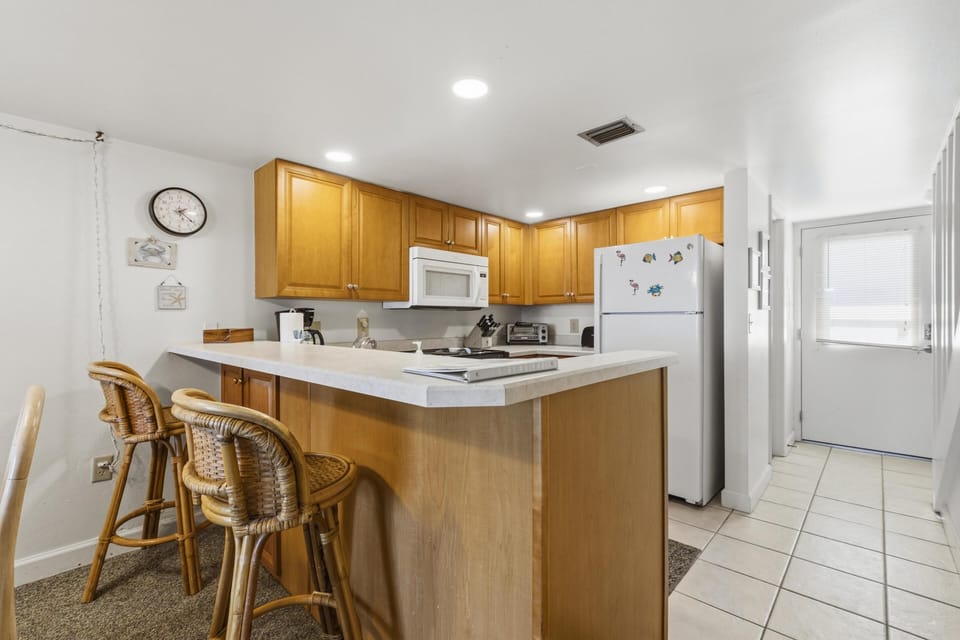 Kitchen with honey wood cabinets, white appliances, and a wraparound counter with rattan bar stools.