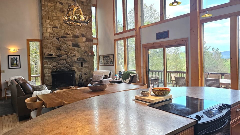 Unwind in this stunning open-concept space where soaring ceilings meet rustic stone fireplace charm. Your kitchen island overlooks the cozy living area, while floor-to-ceiling windows frame breathtaking mountain vistas from your private deck.