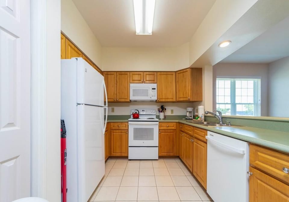 U-shaped kitchen with honey wood cabinets, white appliances, green laminate counters, and tiled floor.