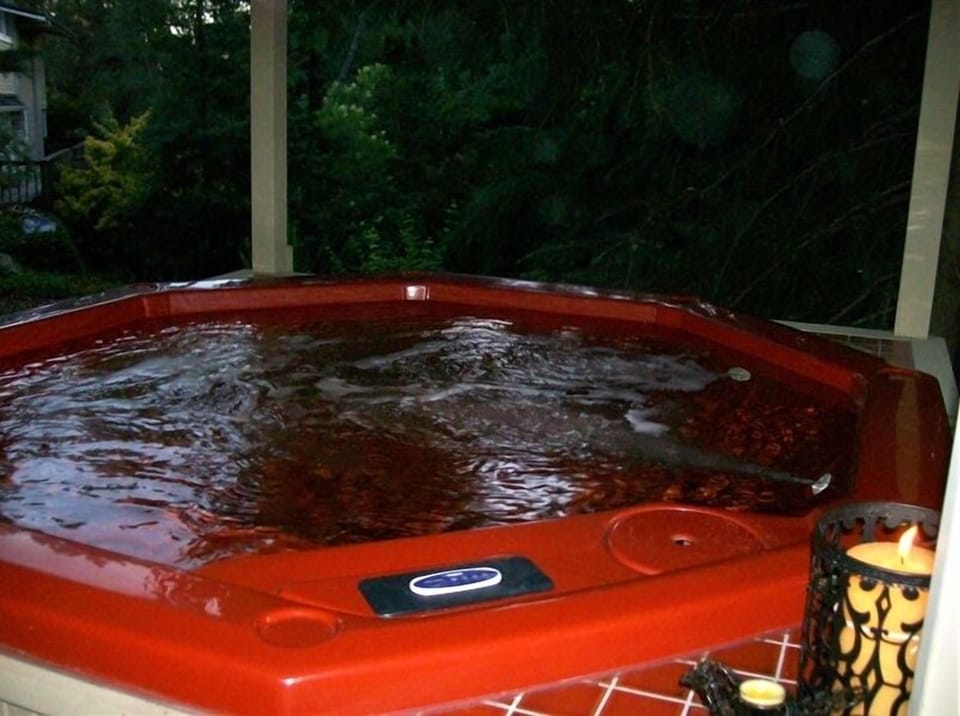 Hot tub perched on deck overlooking yard of many trees & flower gardens.