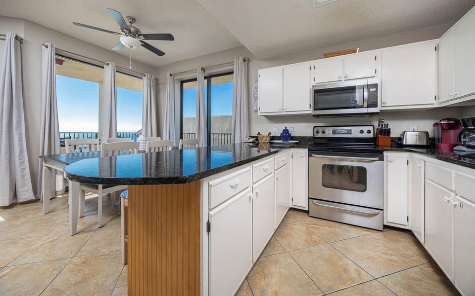 Bright kitchen features a dark countertop, white cabinetry, coffee station, and a dining area with beach views
