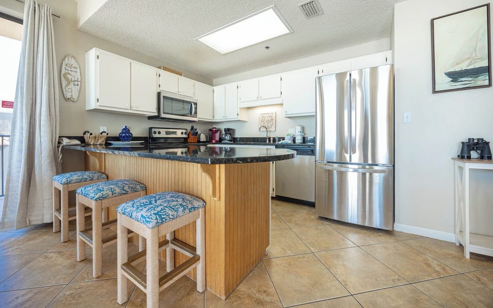 The modern kitchen features a breakfast bar with coral-patterned stools, sleek countertops, and stainless appliances