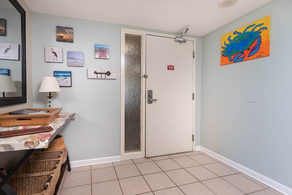 This welcoming entryway features charming coastal artwork, a stylish mirror, and a convenient table for your belongings