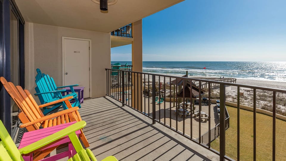 Relax on the vibrant balcony with colorful chairs, enjoying the beautiful view of the beach and sparkling water