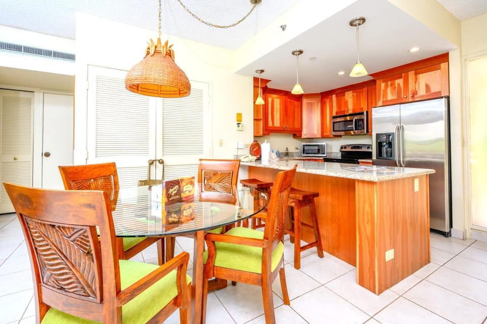 Warm island-style kitchen with granite countertops and tropical dining setup.