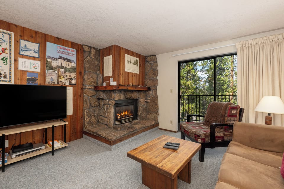 Cozy up in your mountain retreat with a crackling stone fireplace, comfortable seating, and peaceful forest views from your private balcony.