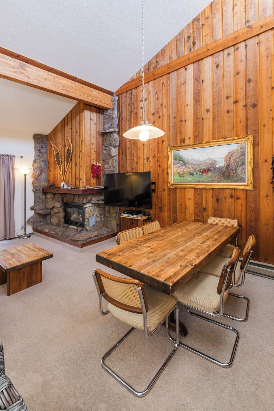 Gather around your rustic dining table beneath warm wood-paneled walls, where a crackling stone fireplace creates the perfect ambiance for memorable meals together.