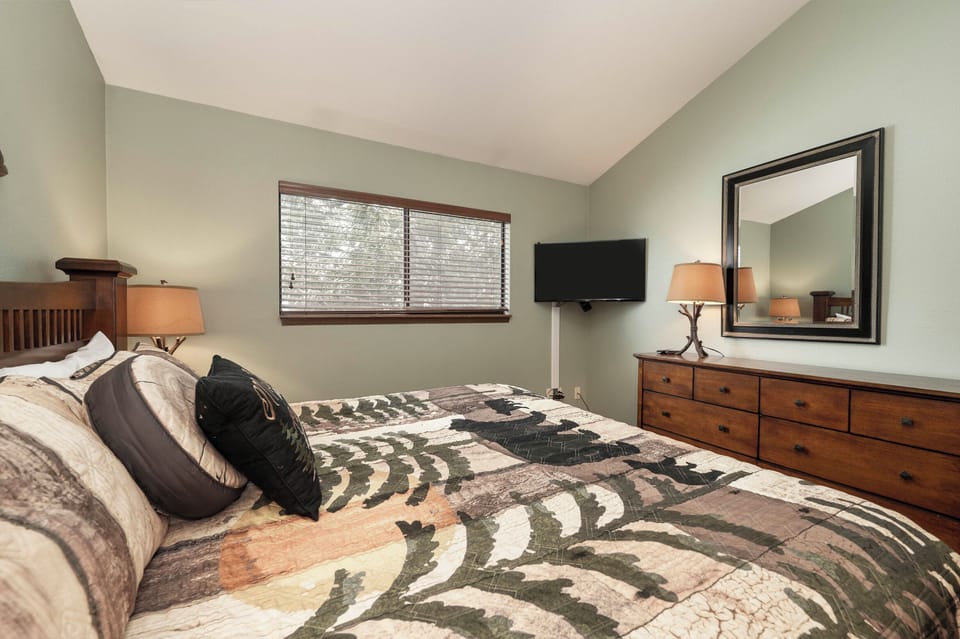 Unwind in your serene bedroom featuring elegant wood furnishings, soft lighting, and a cozy patterned comforter for restful nights.