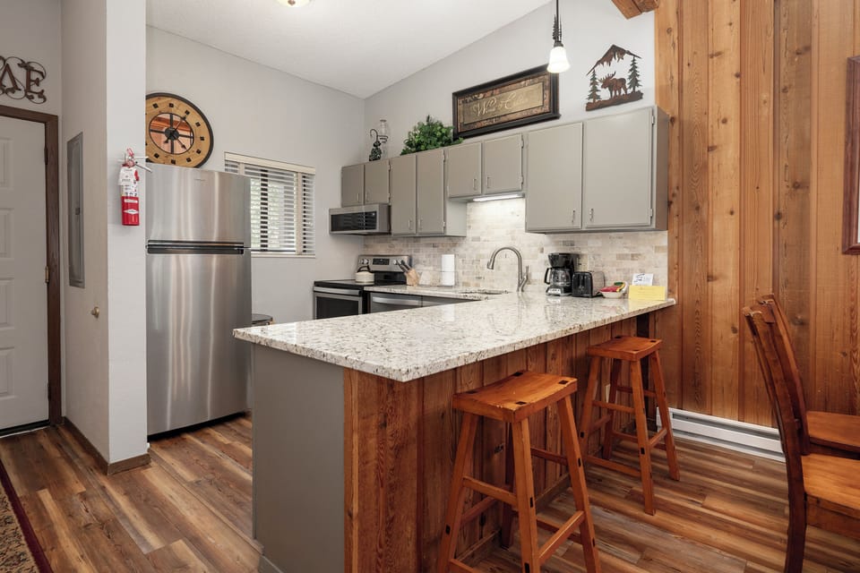 Your fully equipped kitchen features stainless steel appliances, granite counters, and rustic wood bar seating perfect for morning coffee or casual meals.