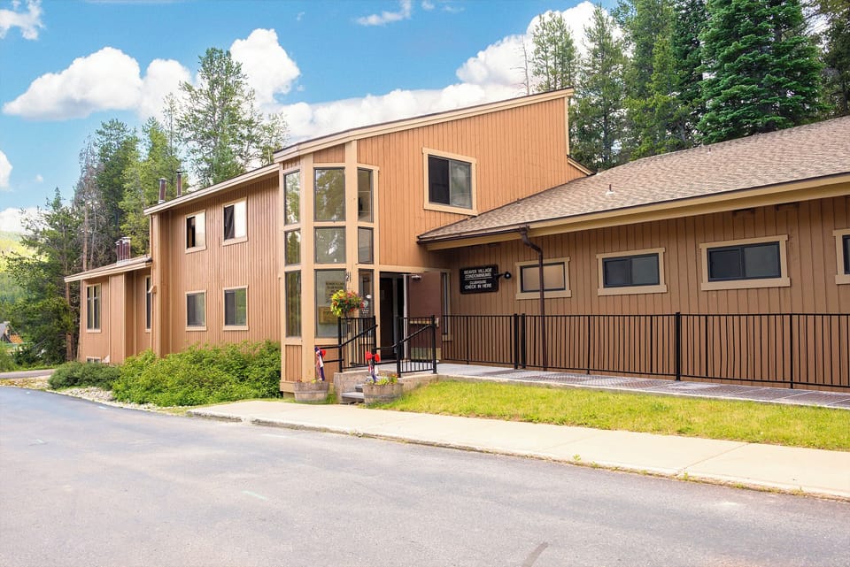 Modern wood-sided property nestled among towering evergreen trees on a quiet residential street.