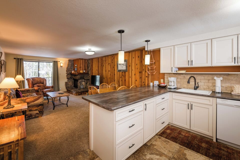 Your open-concept kitchen flows seamlessly into the cozy living area, where rustic wood walls and a stone fireplace create the perfect mountain retreat atmosphere.