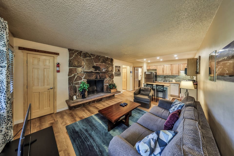 Unwind in your cozy living space featuring a stunning stone fireplace, comfortable seating, and fully equipped kitchen for all your getaway needs.