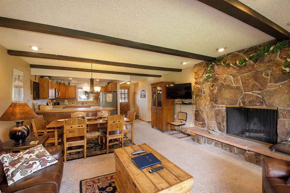 Cozy up in your rustic living space with warm wood beams, stone fireplace, and open kitchen perfect for mountain getaway meals.