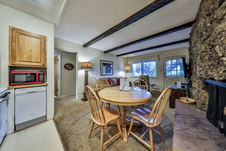 Gather around your cozy dining table beneath rustic exposed beams, where the stone fireplace creates perfect ambiance for memorable meals together.