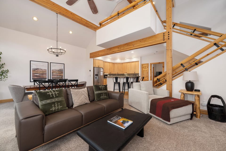 Relax in your spacious open-concept living area featuring vaulted ceilings, warm wood beams, and modern furnishings that create the perfect mountain retreat atmosphere.