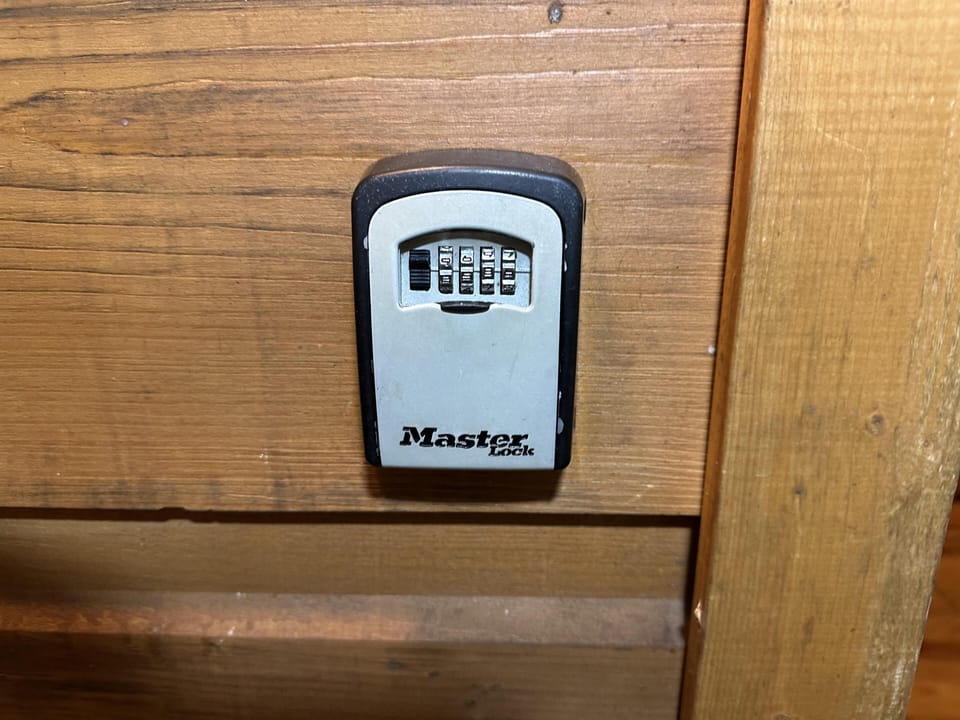 Combination lockbox mounted on a natural wood-paneled wall for secure key storage near the entrance.