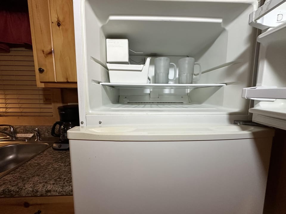 Freezer compartment in the kitchen with two frosted mugs, ice cube tray, and natural wood cabinets nearby.