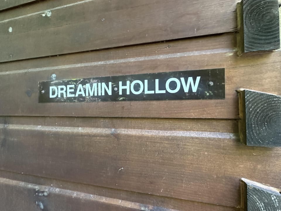 Black metal sign with white lettering mounted on dark stained wooden cabin siding.