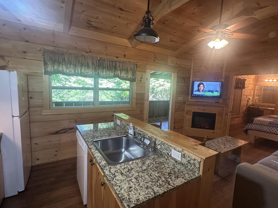 Granite countertop kitchen sink faces a window with forest-patterned valance, overlooking the living area and bedroom.