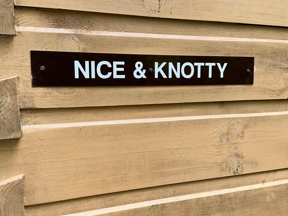 Black metal cabin sign with white lettering mounted on horizontal natural wood logs.