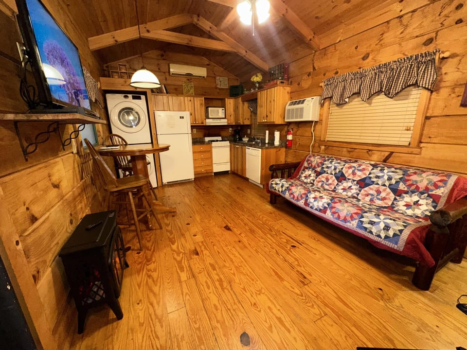 Log-paneled living area with a floral patchwork quilt on a wooden futon and a wall-mounted flat-screen TV.