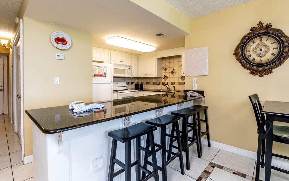 This kitchen features sleek granite countertops, white cabinetry, and a cozy bar area perfect for casual dining