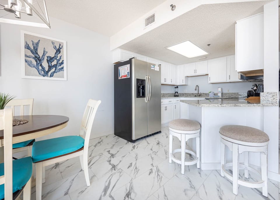 Bright kitchen featuring white cabinetry, stylish countertops, and a breakfast bar with two cushioned stools