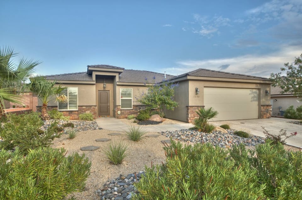 Front of Home with palm trees and purple flowering bushes.