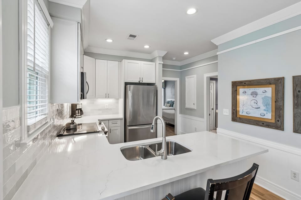 Your spacious kitchen offers everything you need with sleek white countertops, stainless steel appliances, and coastal charm that makes cooking feel effortless.