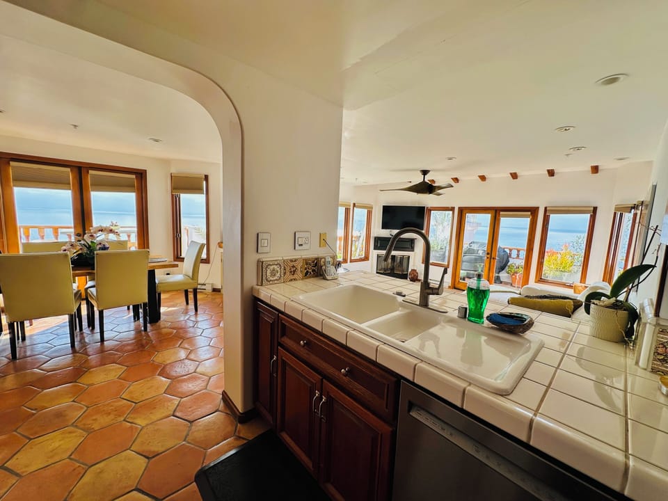 - Cook with a view in this open kitchen overlooking the ocean & sunlit living area
- Classic tiled countertops, wood cabinetry & arched details blend charm & function
- Seamless layout connects kitchen, dining & patio for the ultimate entertaining space