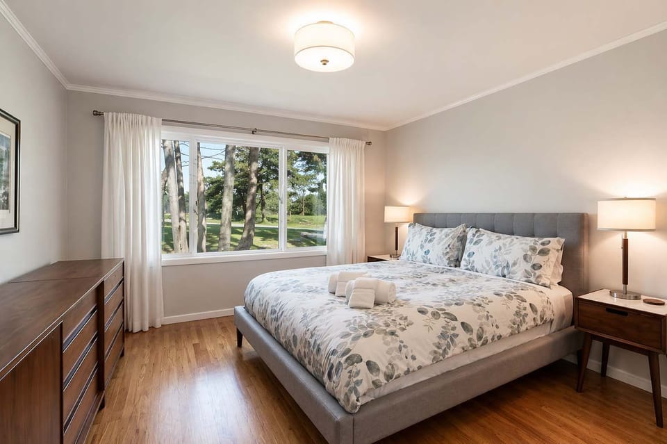 Bright and spacious bedroom with a comfortable bed, warm wood floors, and large windows bringing in natural light.
