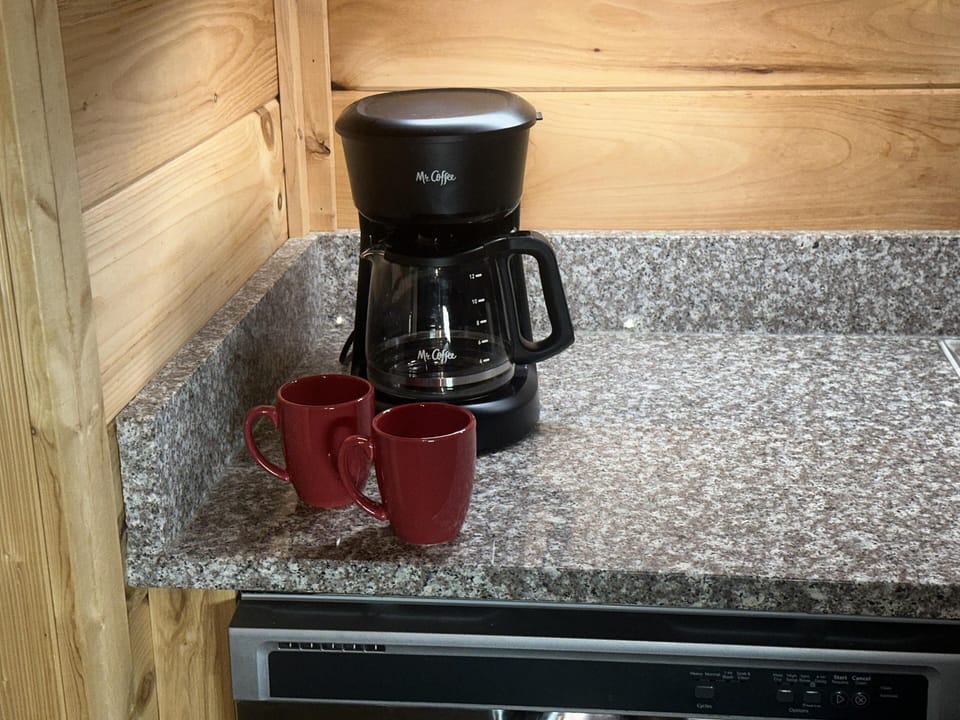 Black drip coffee maker sits on speckled gray granite countertop against natural wood-paneled walls.