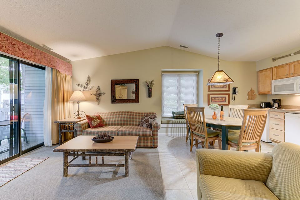 A queen-size sleeper sofa and additional seating in the living room of the unit, complemented by a dining table. The living space extends to a balcony, offering a pleasant garden view.