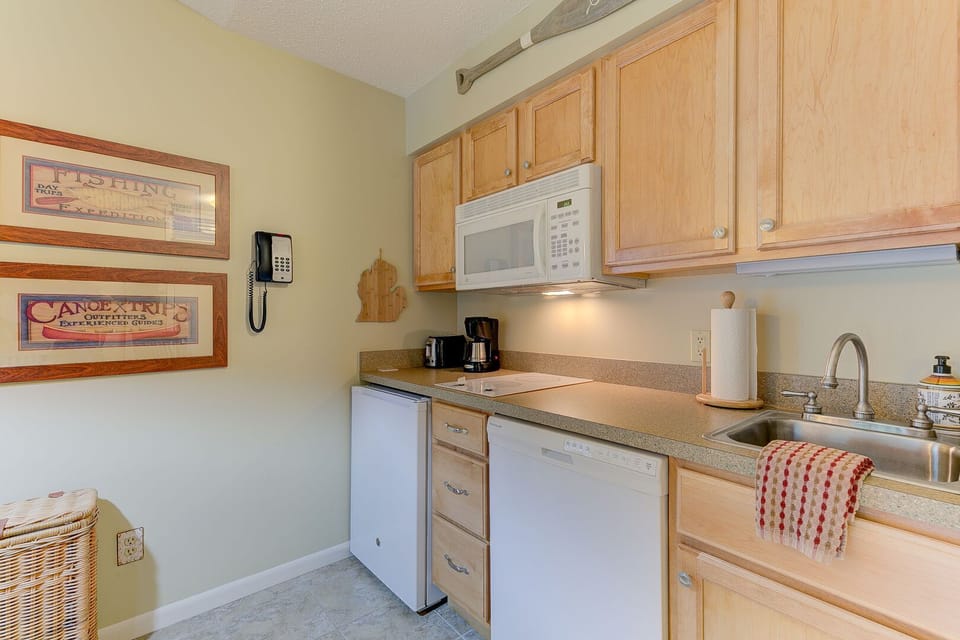 A fully equipped kitchen featuring a coffee maker, stove top, dishwasher, microwave, toaster, pots and pans, tea towels, cooking utensils, silverware, and more.