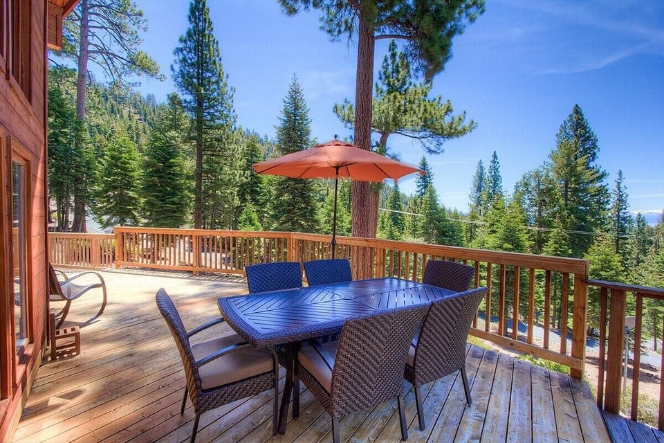 Deck with patio table, chairs, umbrella, railing, trees, forest view, and mountain view.