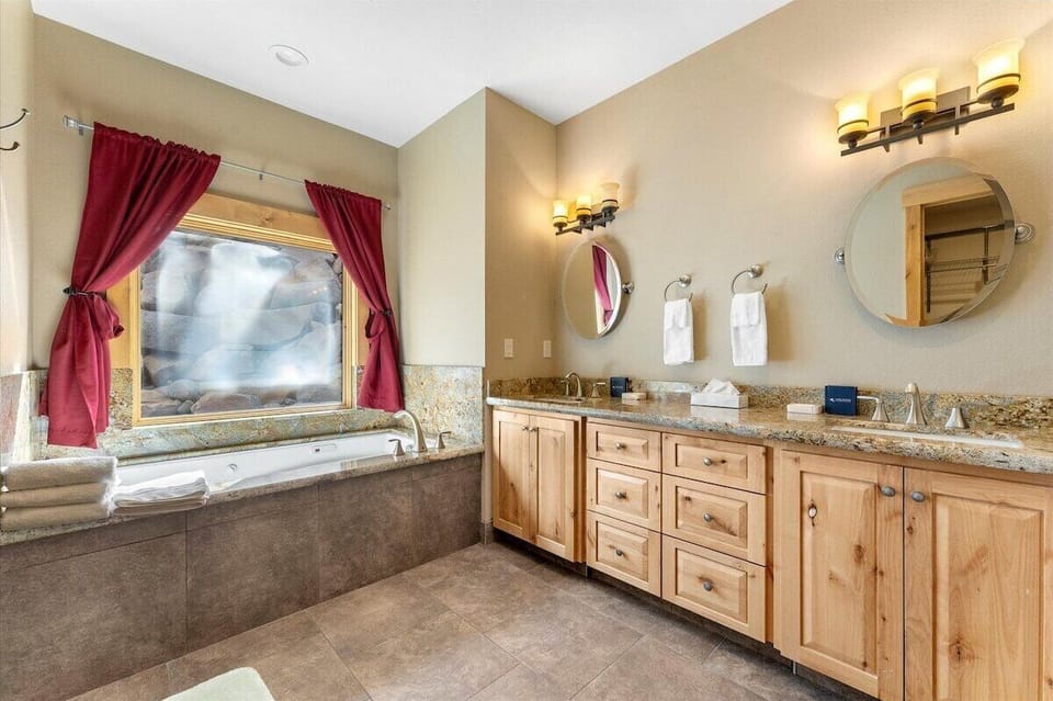 Bathroom with a double vanity, round mirrors and a large tub.