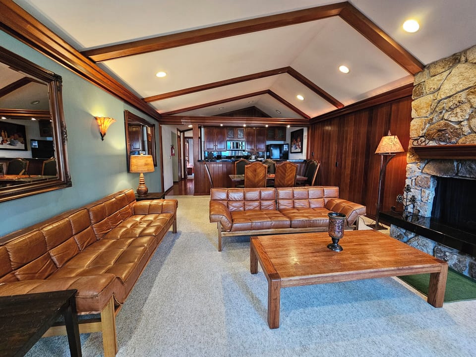 Living room with sofas, coffee table, side tables, lamps, mirror, dining table, dining chairs, and ceiling beams.