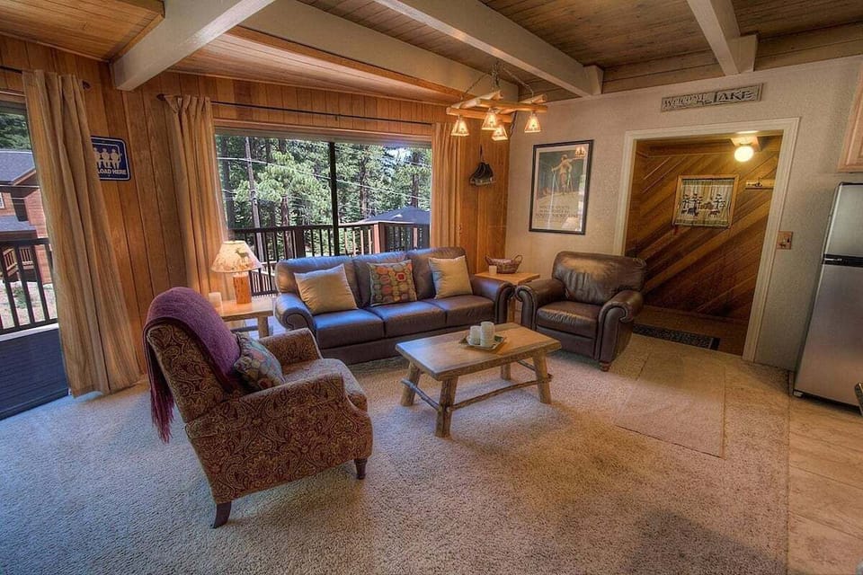 Living room includes sliding door, deck railing, sofa, and armchairs.