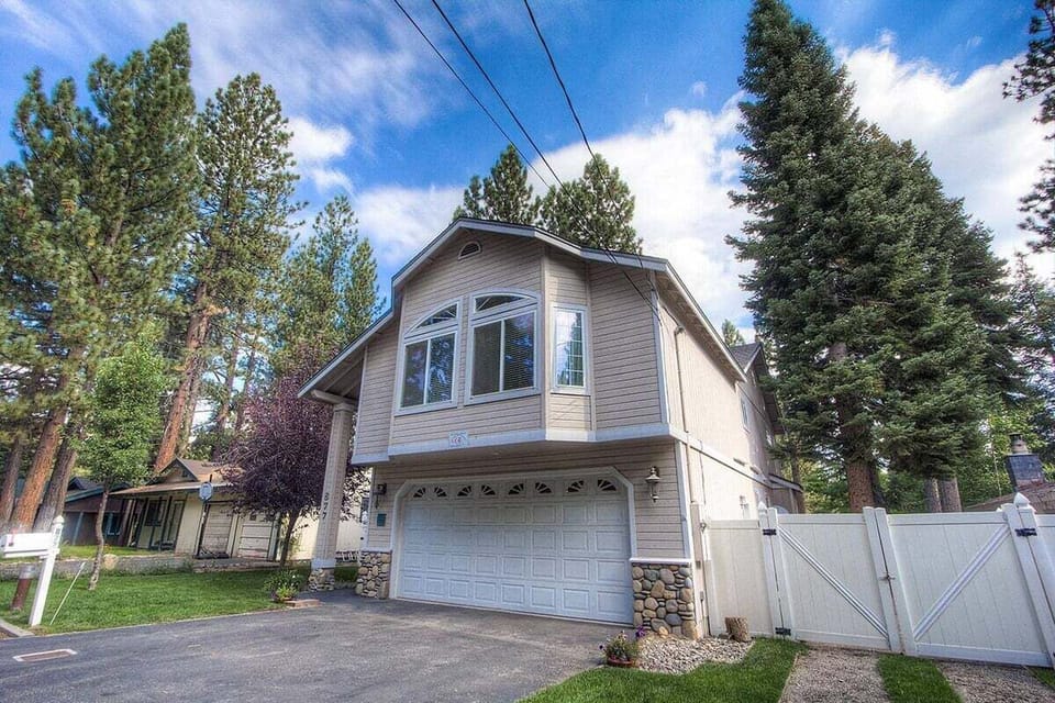 Front exterior with garage door, driveway, fence gate, front entry, windows, and trees.
