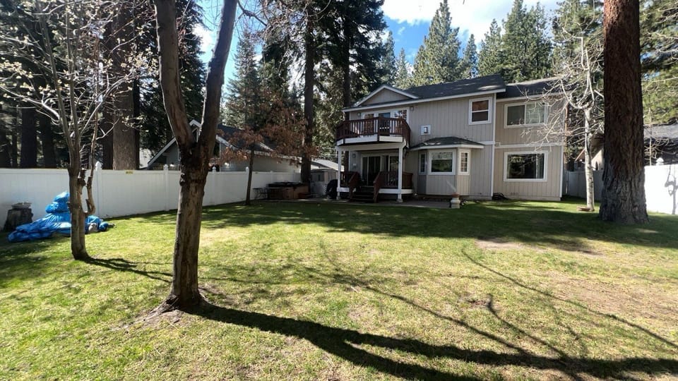 Backyard with rear exterior, balcony, deck, patio, hot tub area, lawn, fence, and trees.