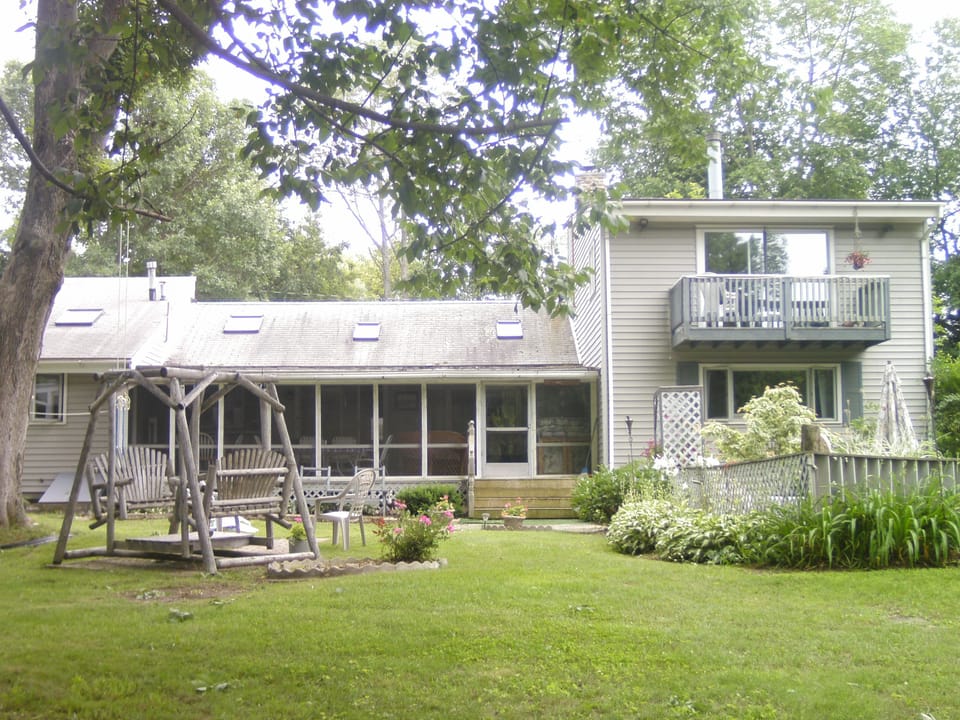 Back of house with double cedar swing, screen porch, gas grill and eating area.