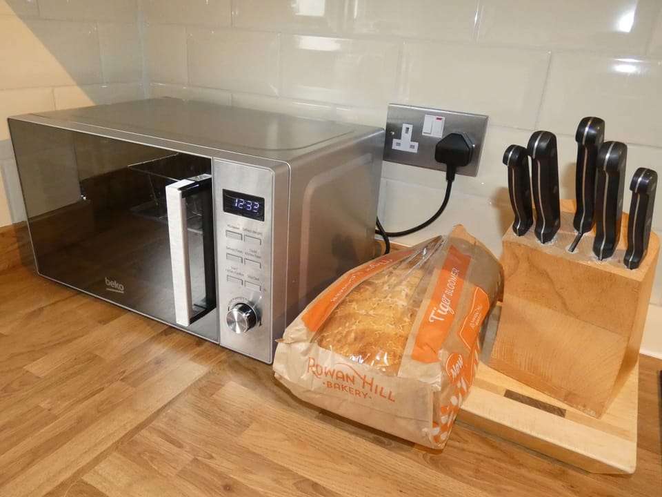 Microwave, knife set, chopping board and a fresh loaf of bread.