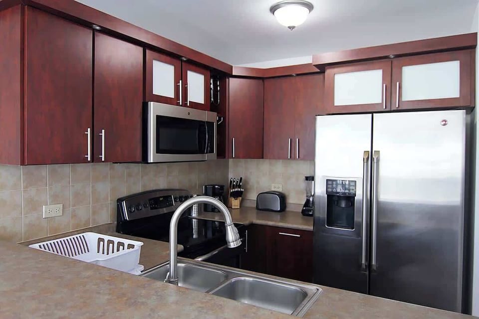 Fully equipped kitchen featuring a refrigerator, stove with oven, microwave, coffee maker, toaster, blender, and complete sets of pots, pans, utensils, silverware, cups, mugs, and plates.
